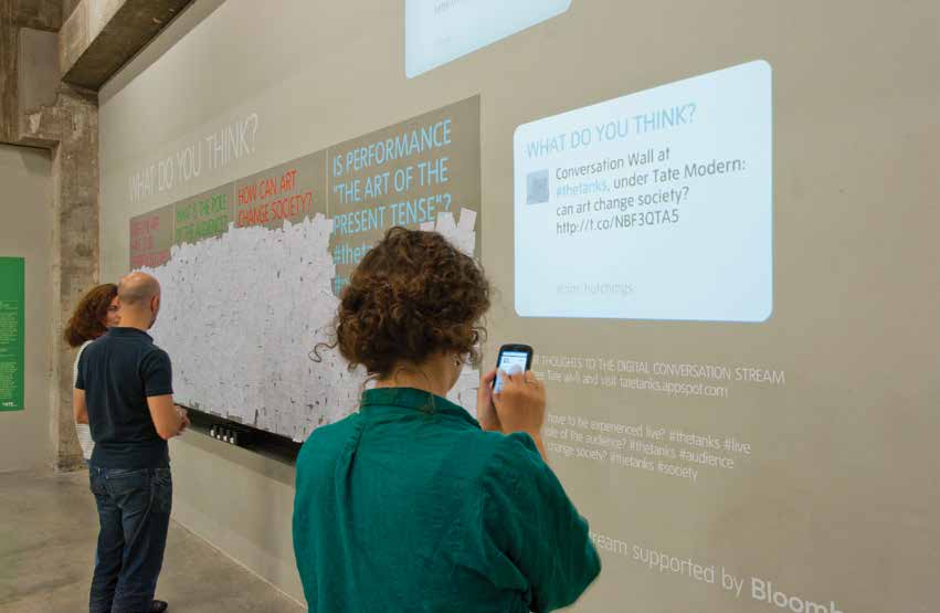 People standing in front of an interactive wall with their smart phones showing what they are tweeting about. 