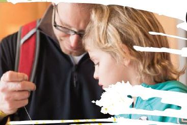 A father and daughter look down on a craft they are making.
