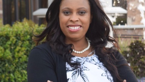 Woman stands outside with her arms crossed smiling
