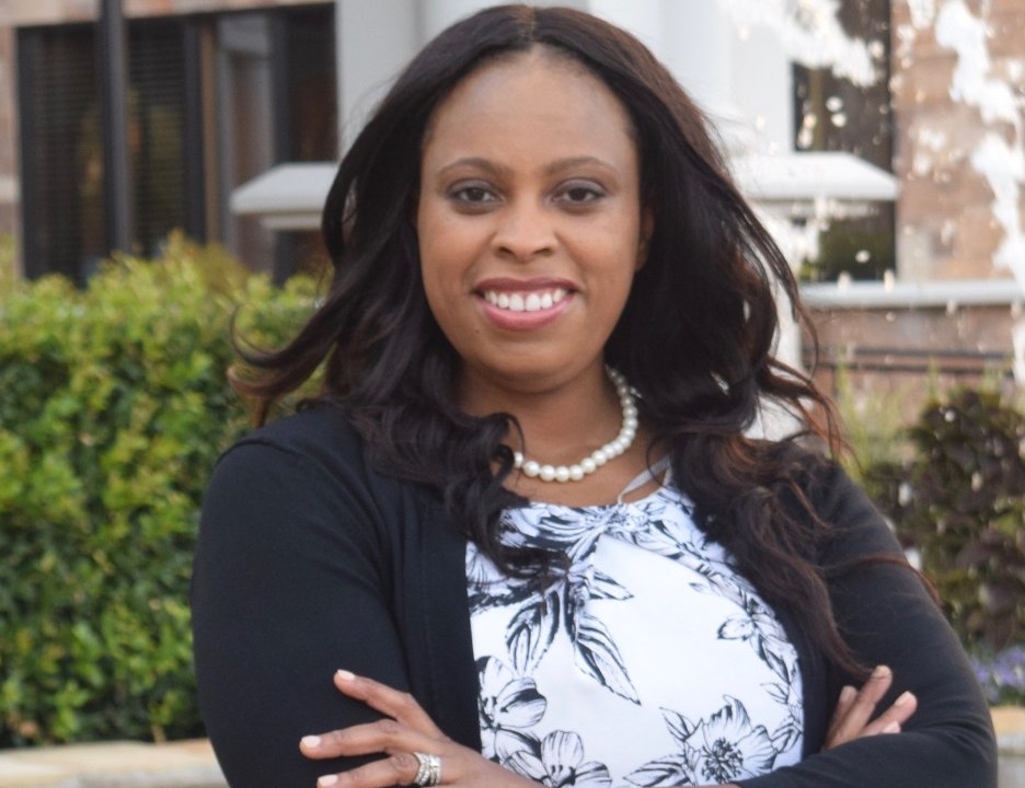 Woman stands outside with her arms crossed smiling