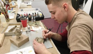 Collin Moret, an assistant preparator, consults a field guide and "study skin" taxidermy mount while painting a sandpiper model.