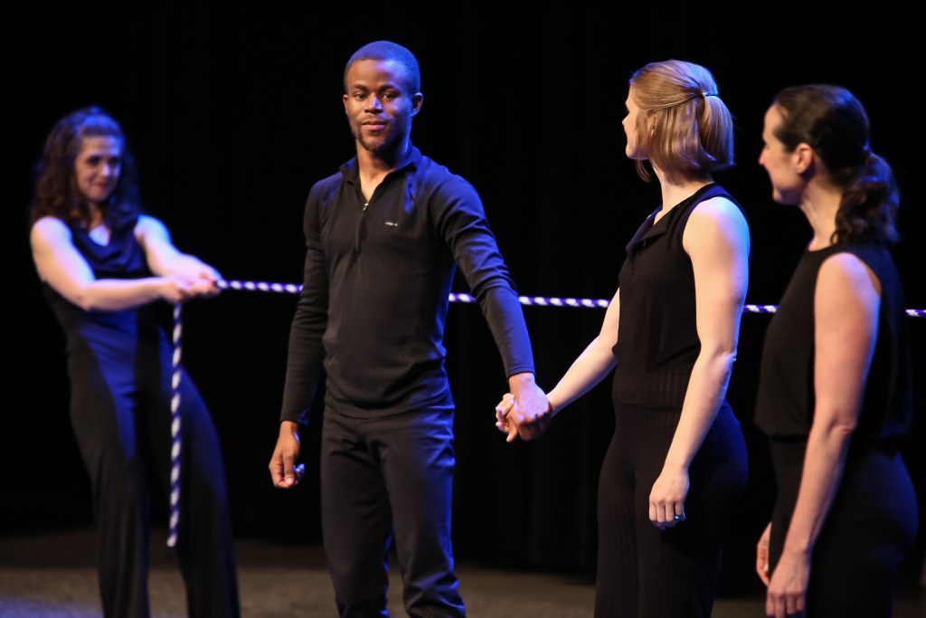 Image of four people, two holding hands in the center of a stage