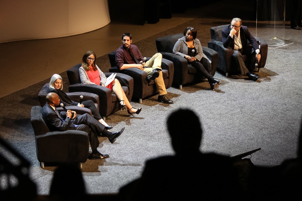 Six people sitting in chairs on a stage