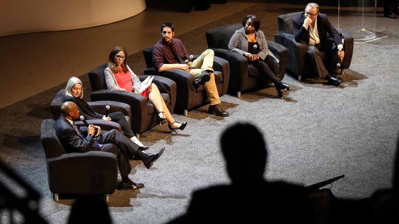 Six people sitting in chairs on a stage