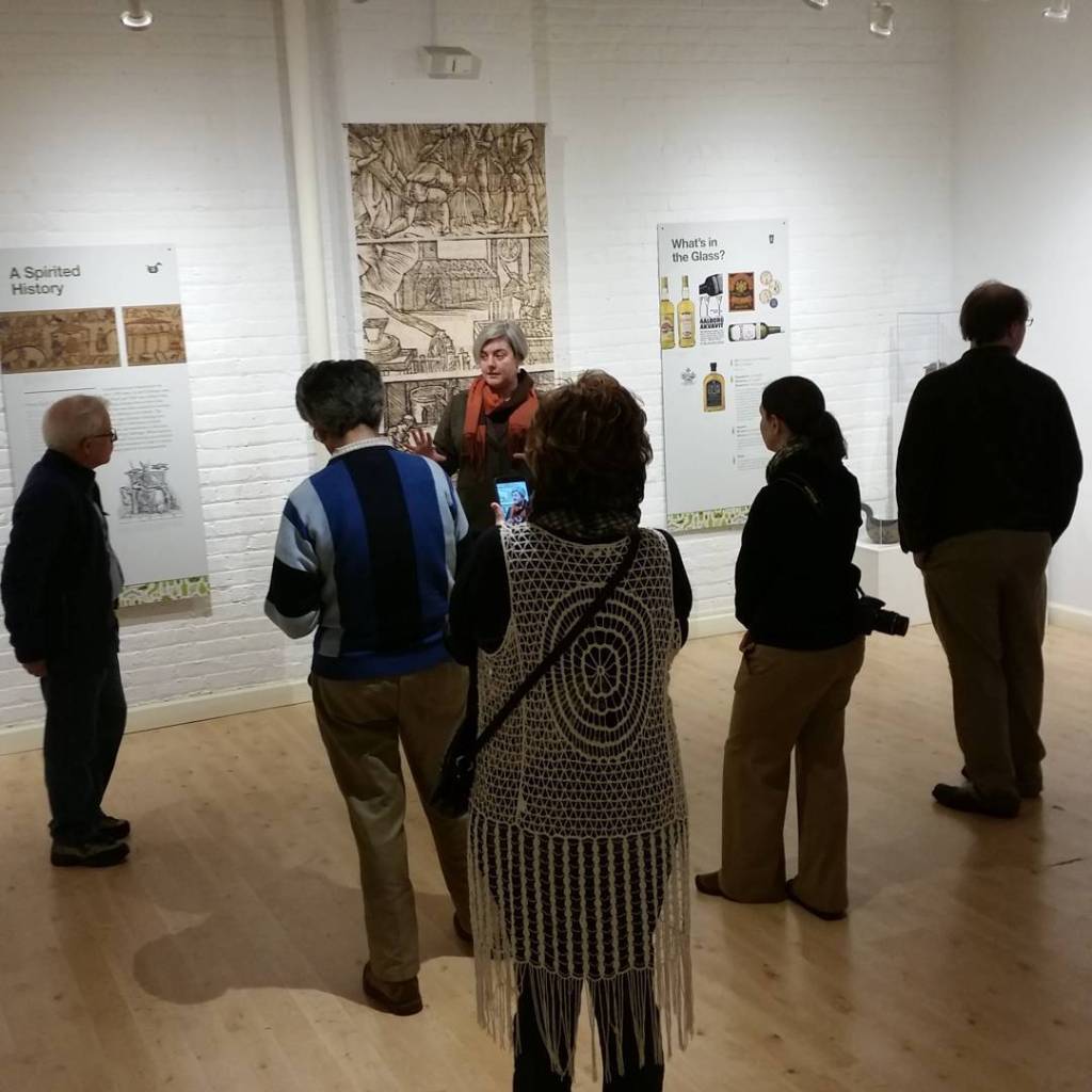 Group of people in a white walled gallery listening to a curator speak