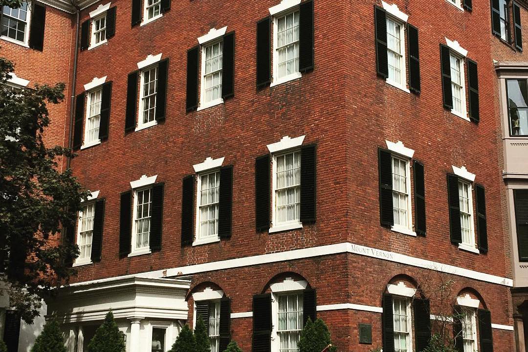 View of courtyard entrance to a red brick building with black shutters.