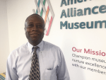 Image of man in shirt and tie standing in front of the AAM logo