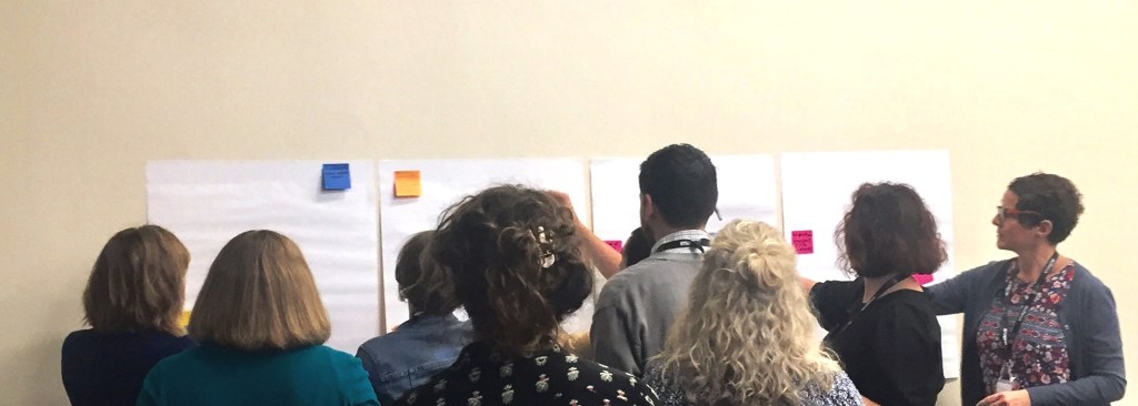 Group of people with their backs to the camera adding comments to several flipchart pages stuck to a wall