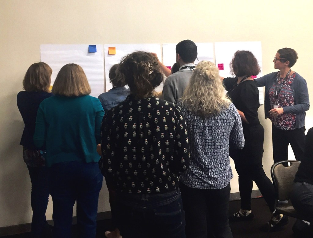 Group of people with their backs to the camera adding comments to several flipchart pages stuck to a wall