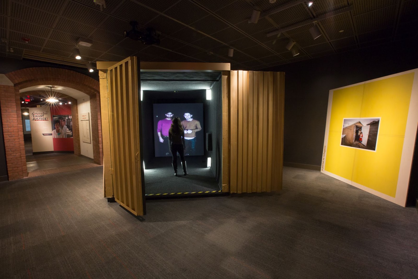 Image of a shipping container with a video portal at the far end of it and a person inside talking to two other people from the portal