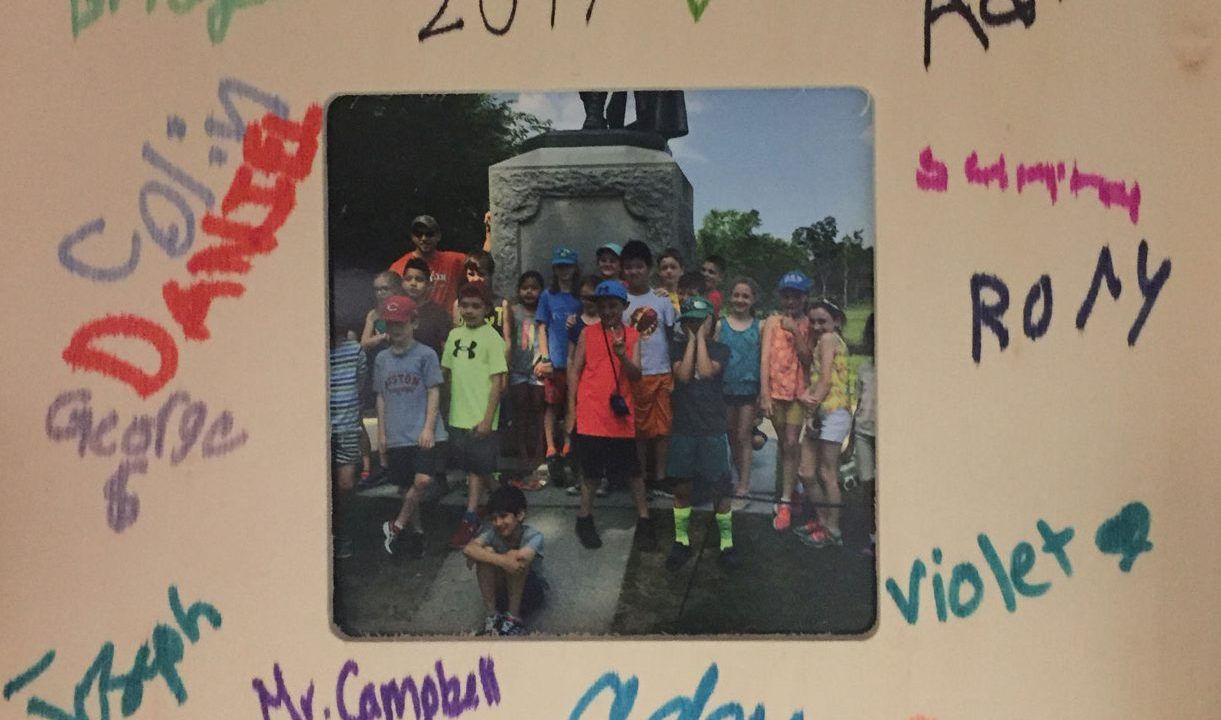 Group of children surrounding a statue framed with mat signed by all of the kids