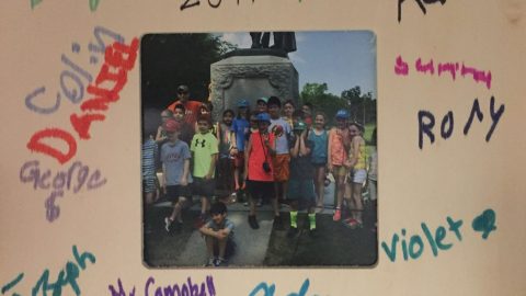 Group of children surrounding a statue framed with mat signed by all of the kids