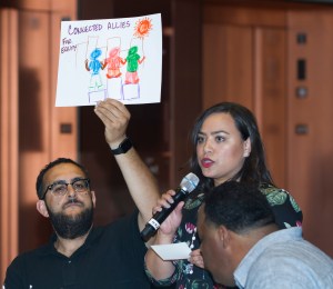 A woman stands in front of a group of individuals holding up a poster