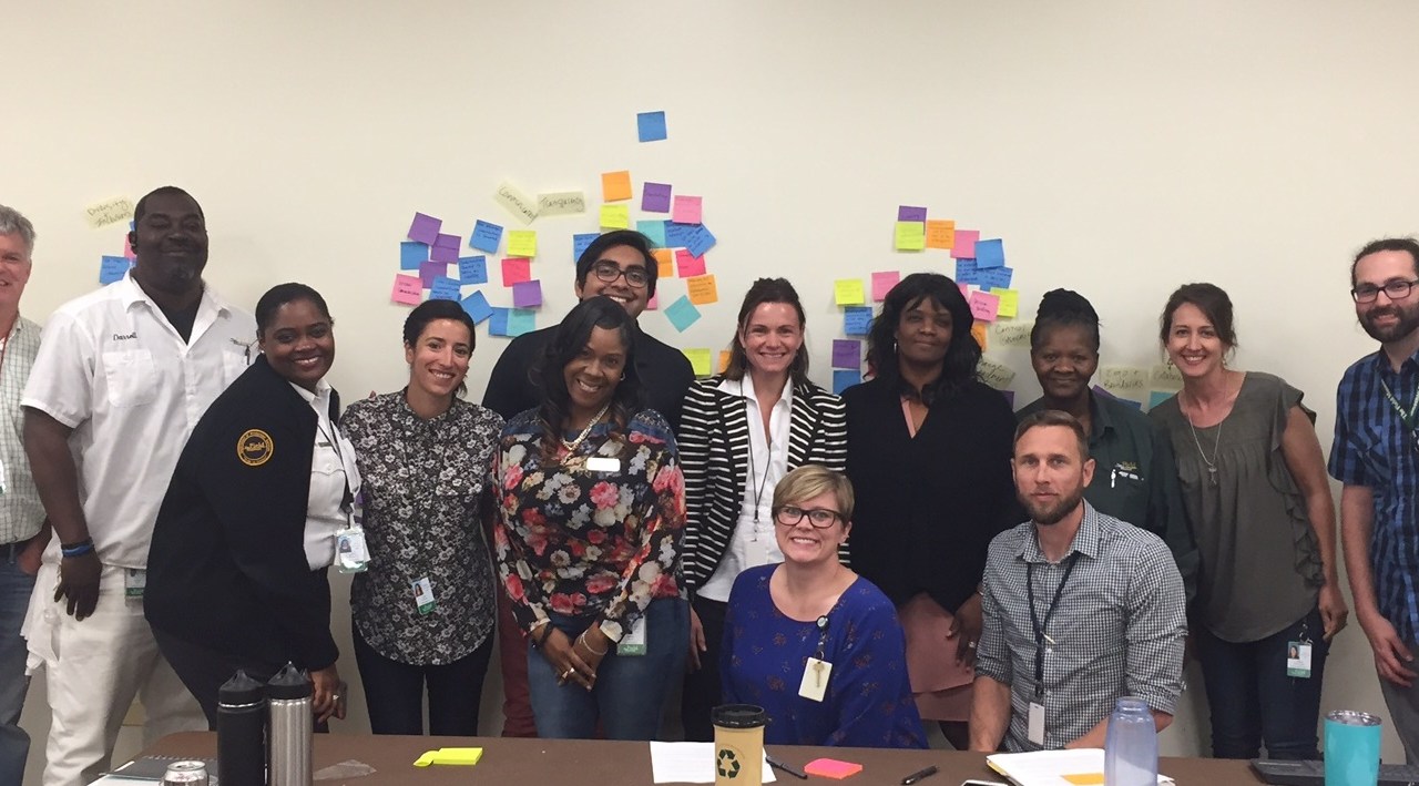 Group of diverse individuarls standing and sitting in front of a white wall with post-it notes on it