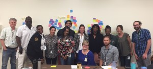 Group of diverse individuarls standing and sitting in front of a white wall with post-it notes on it