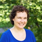 Woman smiling with short curly brown hair wearing a blue shirt