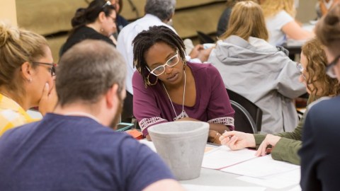 Young woman sits at a table intently looking at papers with several other people around her