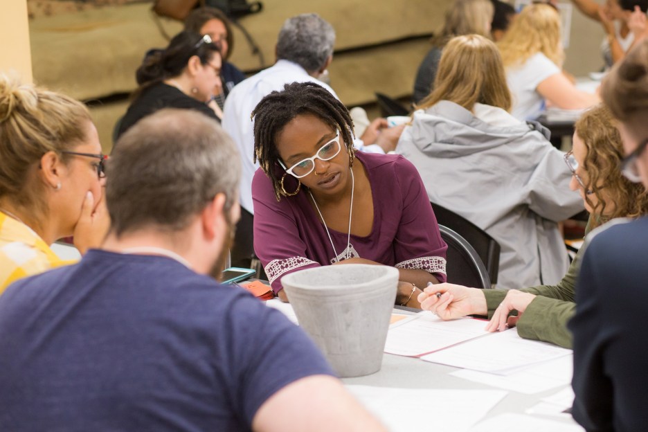 Young woman sits at a table intently looking at papers with several other people around her