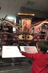 Small child holds a photo of a fire truck up while standing in front of a fire pumper.