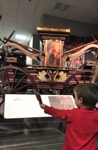 Small child holds a photo of a fire truck up while standing in front of a fire pumper.