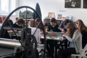 A group of students sit around a table. A round industrial looking wheel sits in the foreground.