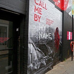 Exterior shot of the Call Me By My Name exhibit written on a brick wall outside the gallery