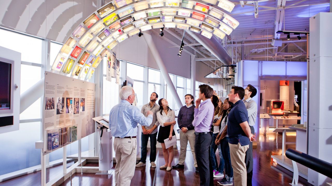 A man leads a group of people on a tour they stand under an arched lighted structure