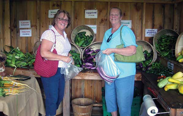 Two women stand in front of a vegetable stand