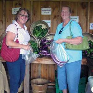 Two women stand in front of a vegetable stand