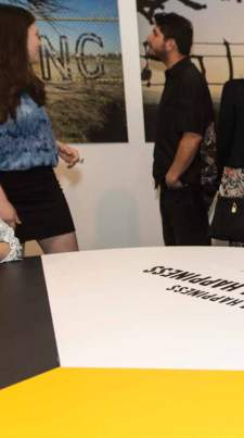 Several people mull around looking at various pieces on art on the wall with a table in the foreground that says Happiness in all capital letters.