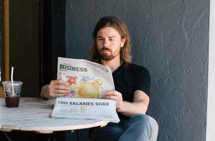 A man sits a table reading a magazine that says CEO salaries soar