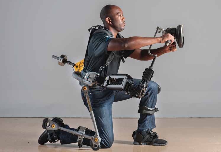 A man kneels on one knee and holds his arms out in front of him wearing an exoskeleton enabling him to do so.