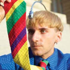 A man holds his multi-colored rainbow tie up while an antenna like apparatus extends from his head.