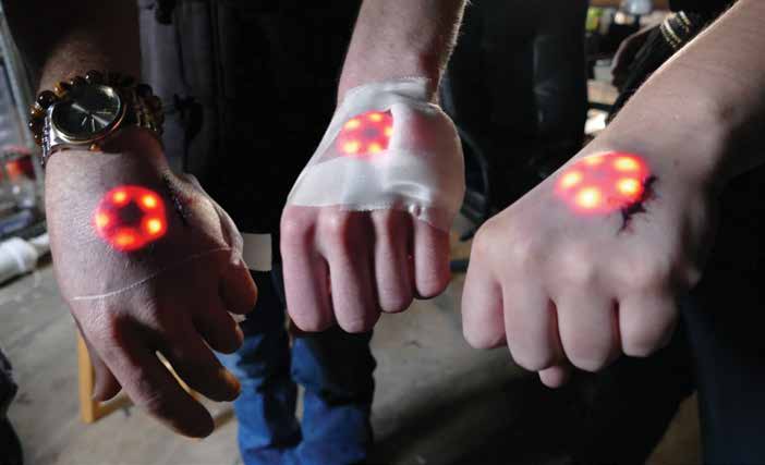 Three people hold their hands out to show lighted implants under the skin on the backs of their hands. 