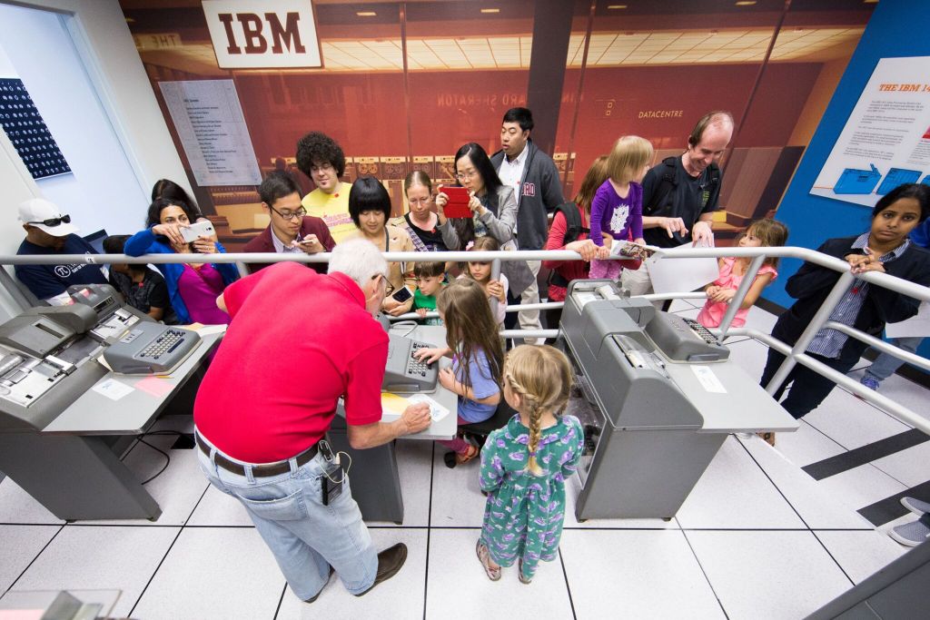 A docent in a red shirt tells a group of people about a display