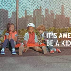 A group of children sit next to a chainlink fence wearing wristbands