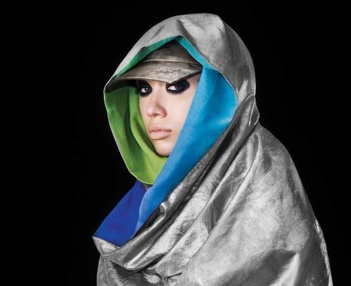 A woman wearing a metallic fabric scarf on her head and shoulders looks into the camera