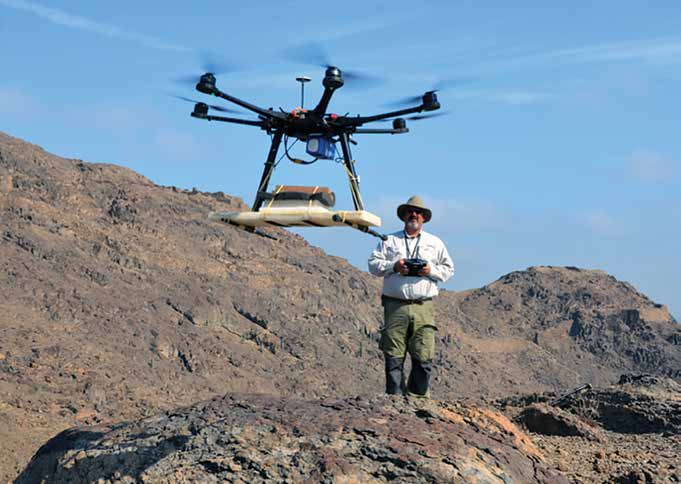 A man stands on a rocky hillside controlling a large drone in the foreground