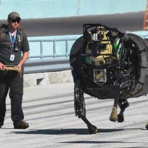 A man controls a large headless robot running down a road