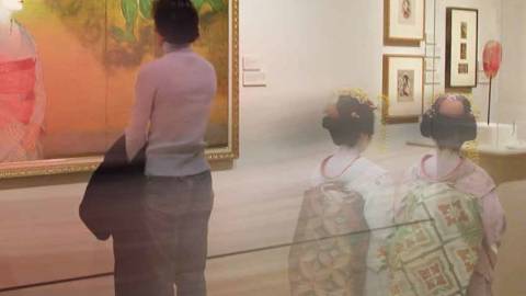 A man stands looking at an Asian artwork while two women dressed in traditional Geisha garb walk behind him