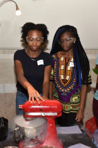Two teens work with a mixer wearing safety goggles
