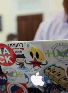 A man stis working on a laptop covered in hacking stickers