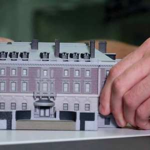 Someone's hands manipulate a miniature building