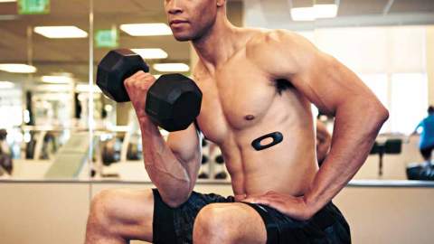 A man sits on a workout bench holding a dumbbell and an AmpStrip