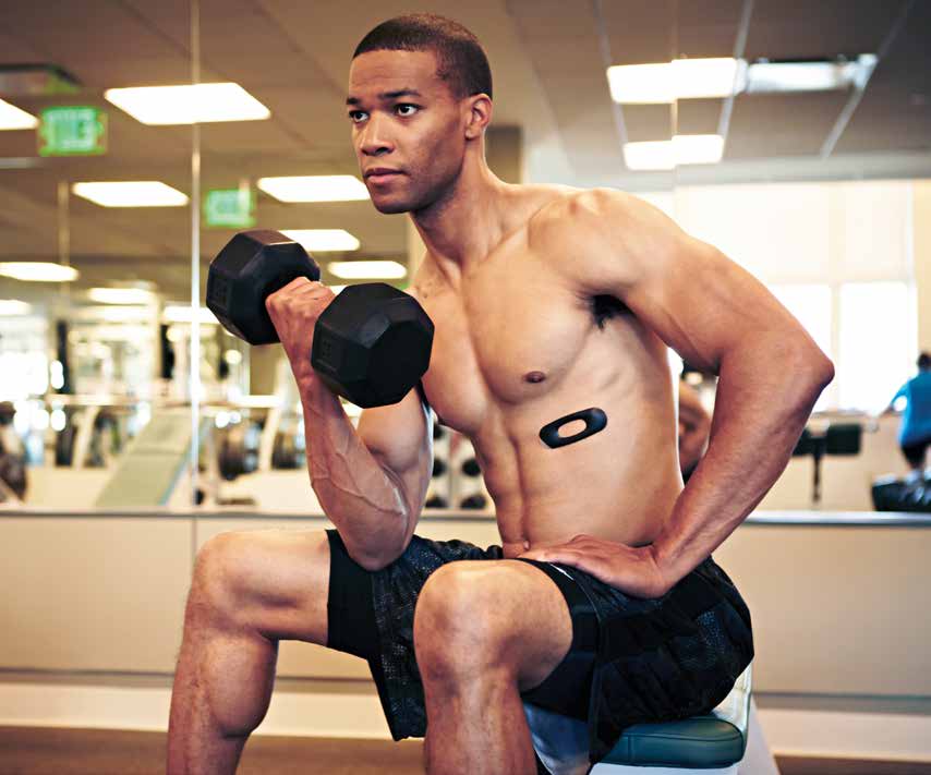 A man sits on a workout bench holding a dumbbell and an AmpStrip