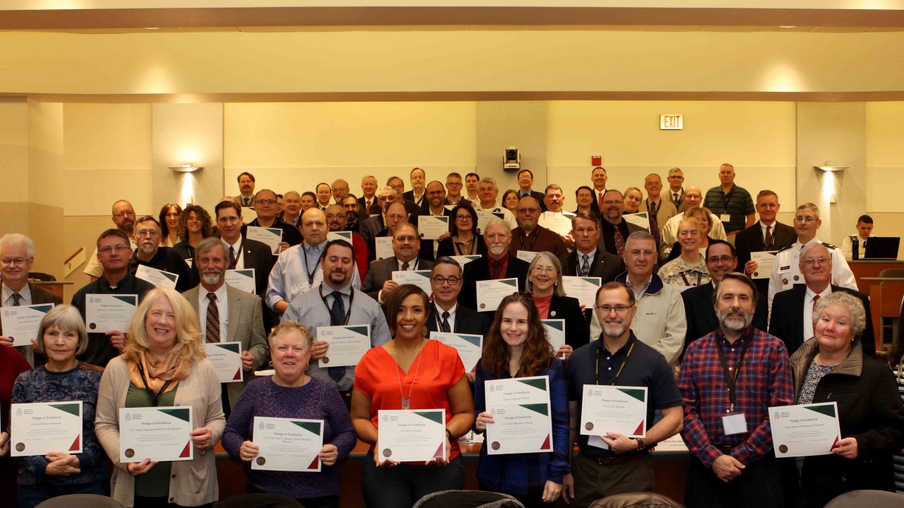 A group of people stand in an auditorium holding up certificates