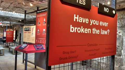 Image of a text panel in red with yes and no arrows pointing to different routes through the exhibit with the question "Have you ever broken the law?"