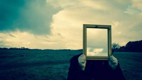 A person holding up a mirror backwards where it shows the sky instead of a face.
