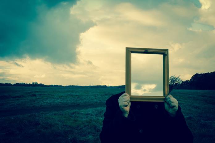 A person holding up a mirror backwards where it shows the sky instead of a face.