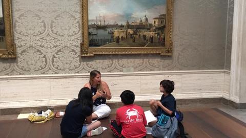 Field trip to the National Gallery with children sitting on the floor in front of a painting with a teacher sitting and interpreting